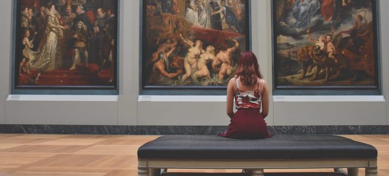 A woman sitting in front of a row of paintings.