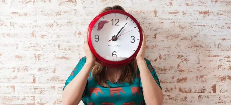 Woman holding a clock in her hands in front of her face