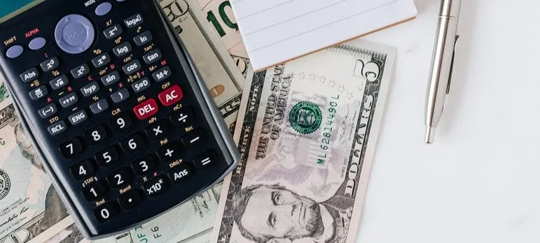 Calculator and a notepad next to a pile of US dollars