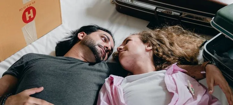 A couple on the bed with two suitcases and a moving box