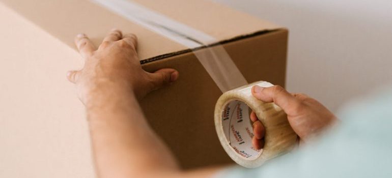 person closing a moving box with a tape