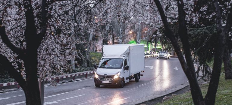 a white moving truck and trees in flower surrounding it