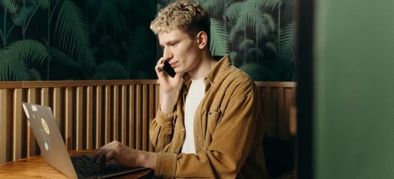  man talking on the phone while tyoing something on the laptop 