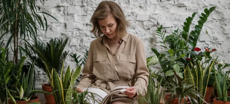 A woman is reading a book while surrounded by plants.