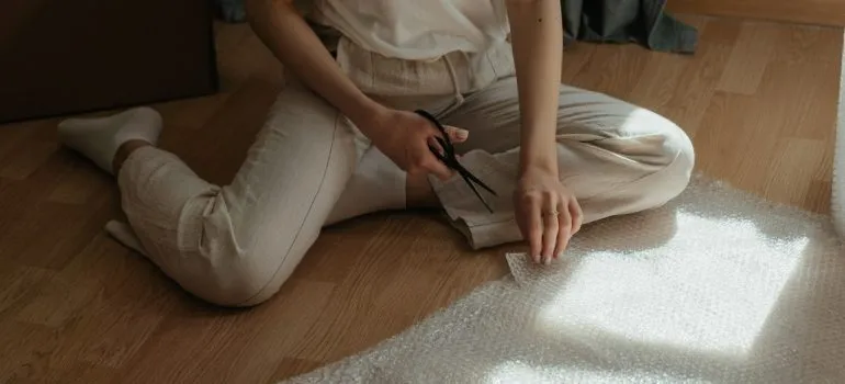 Woman in white pants cutting bubble wrap