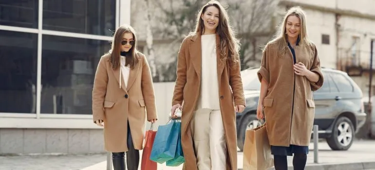Three women in coats are walking in town and carrying shopping bags. 