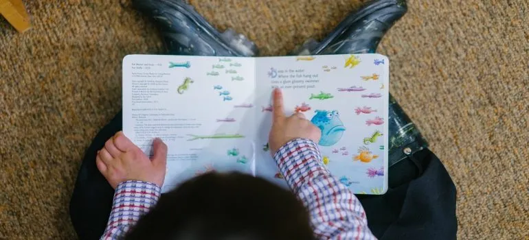 a toddler pointing at something in a book while sitting on the floor