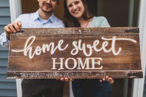 A couple holding a wooden sign "Home sweet home"