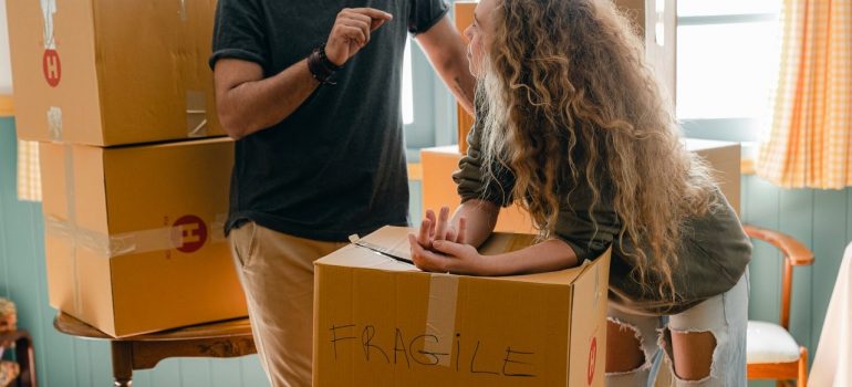 a woman leaning on a cardboard box that says "fragile" while talking to a man