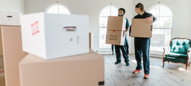two moving crew personnel carrying cardboard boxes in an empty home