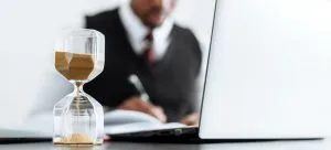 a man sitting in his office in front of a laptop and an hourglass, to represent one of the reasons why you need professional moving assistance
