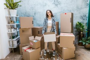 Woman in black and white checkered shirt standing beside cardboard boxes